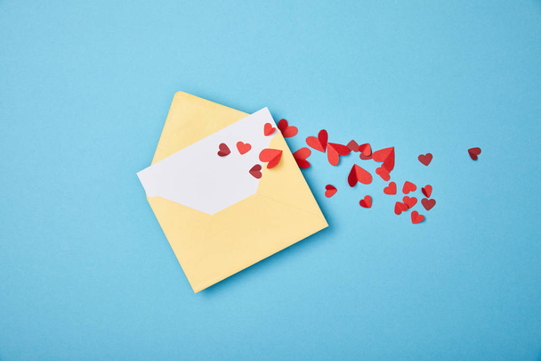 enveloppe jaune avec carte blanche vierge et coeurs coupés en papier sur fond bleu
 - Photo, image