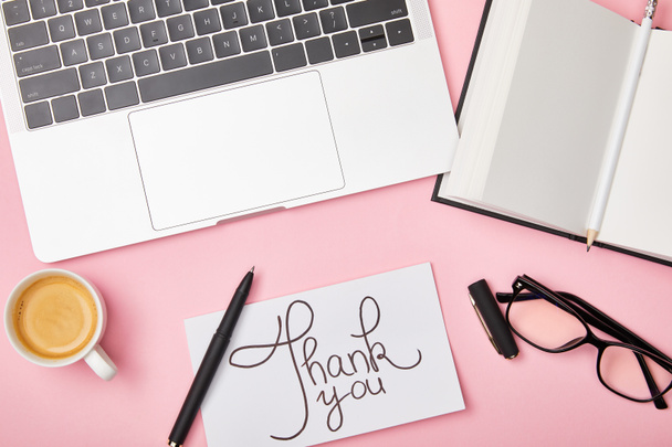 vista dall'alto di laptop, caffè, notebook, occhiali e biglietto con scritte di ringraziamento sul posto di lavoro su sfondo rosa
 - Foto, immagini