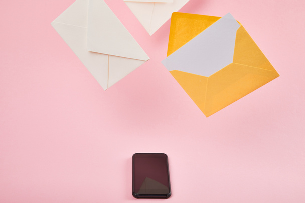 yellow envelope with blank white card near letters and smartphone with blank screen on pink background - Photo, image