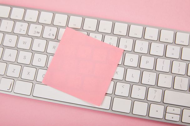 bovenaanzicht van lege roze Sticky Note op laptop toetsenbord op roze achtergrond - Foto, afbeelding