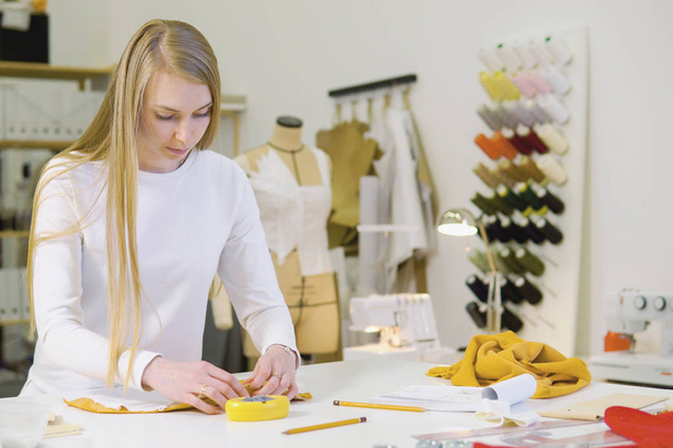 woman with blond hair - freelancer, fashion designer or tailor working on a design or draft with colorful fabrics in workshop. Front view - Photo, Image