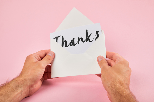cropped view of man holding envelope and white card with thanks lettering on pink background - Foto, Imagem