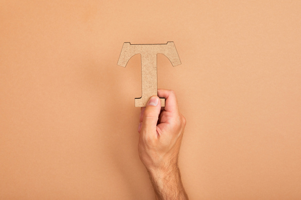 cropped view of man holding paper cut letter T on beige background - Fotografie, Obrázek