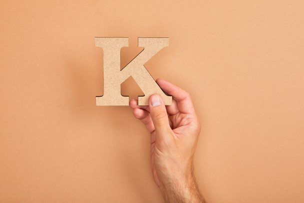 cropped view of man holding paper cut letter K on beige background - Foto, Imagem