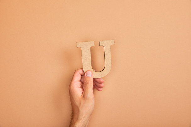 cropped view of male hand holding paper cut letter U on beige background - 写真・画像