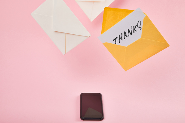envelope amarelo com cartão branco com letras de agradecimento perto de letras e smartphone com tela em branco no fundo rosa
 - Foto, Imagem