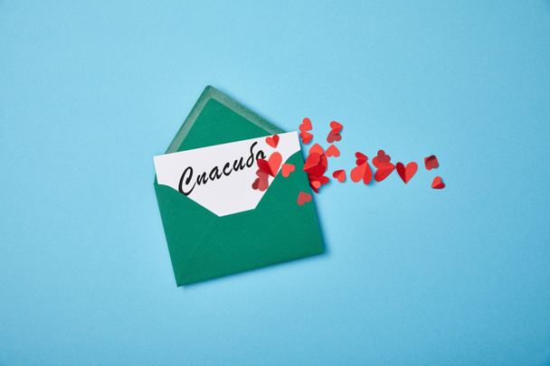 green envelope with thanks lettering in Russian on white card and red paper hearts on blue background - Photo, Image