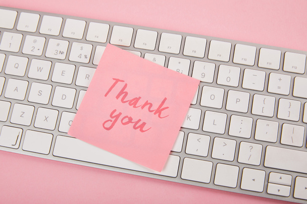 top view of pink sticky note with thank you words on laptop keyboard on pink background - Photo, Image