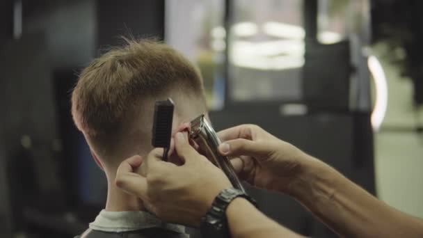 Male haircut with electric razor. Close up of hair trimmer hairstyle. Barber makes haircut for client at the barber shop by using hairclipper. Man hairdressing with electric shaver. Handheld shot. 4K. - Materiaali, video