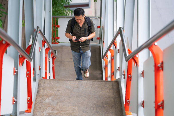 Man walking up stairs and using smartphone in city - 写真・画像