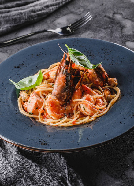 Ζυμαρικά σπαγγέτι με θαλασσινά, λαγουστίνη, μύδια, στρείδια, γαρίδες, φιλέτο σολομού σε σάλτσα με βότανα σε πιάτο πάνω από σκούρο γκρι φόντο. Ιταλικό φαγητό, κορυφαία θέα - Φωτογραφία, εικόνα
