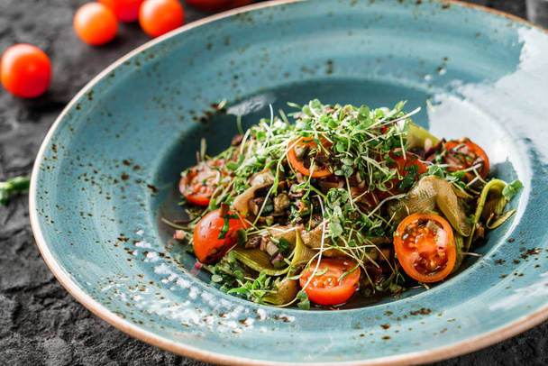 Zdravý veganský salát s olivami, cibulí, cuketou, cherry rajčaty, klíčky v keramickém talíři na tmavém pozadí. Zdravé jídlo, vegetariánská strava, zblizka - Fotografie, Obrázek