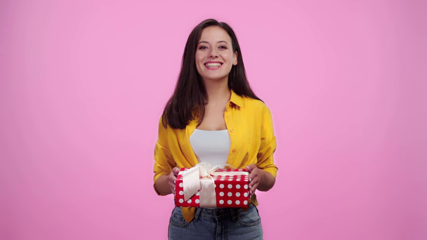 Zeitlupe von schönen Mädchen schüttelt Geschenk, lächelt und schaut in die Kamera isoliert auf rosa - Filmmaterial, Video