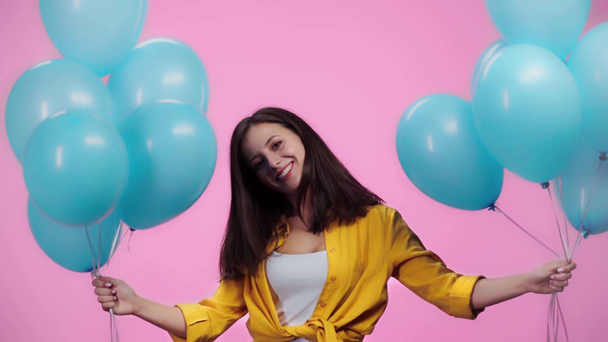 mooi meisje met ballonnen schudden hoofd, kijken naar camera en glimlachend geïsoleerd op roze - Video