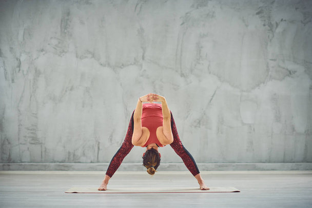 Adatto bruna caucasica in abbigliamento sportivo in piedi sul tappeto esercizio in studio e facendo la posa di yoga a gambe larghe piega in avanti
. - Foto, immagini