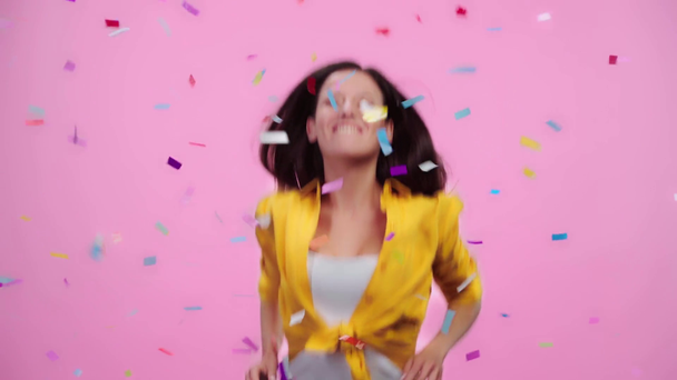 opgewonden mooi meisje kijken naar vallende confetti, lachen en springen geïsoleerd op roze - Video