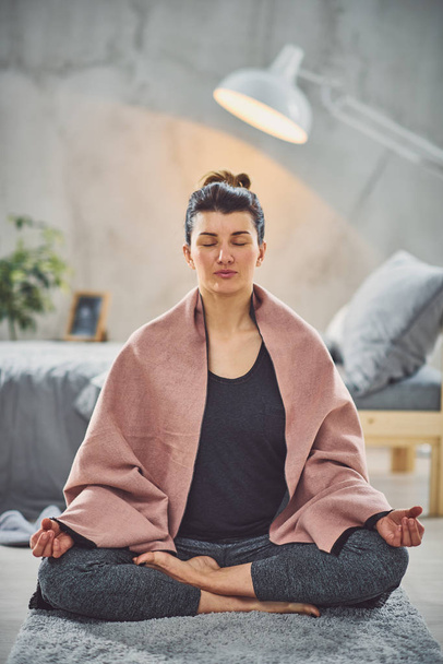 Красивая брюнетка-кавказка сидит на ковре в спальне в позе йоги Лотоса
. - Фото, изображение