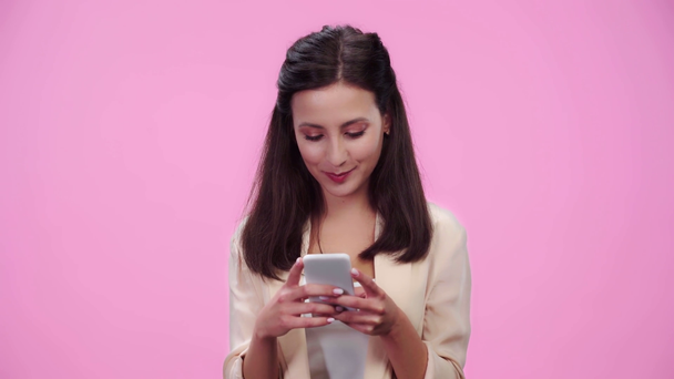 beautiful girl using smartphone and smiling isolated on pink - Filmagem, Vídeo