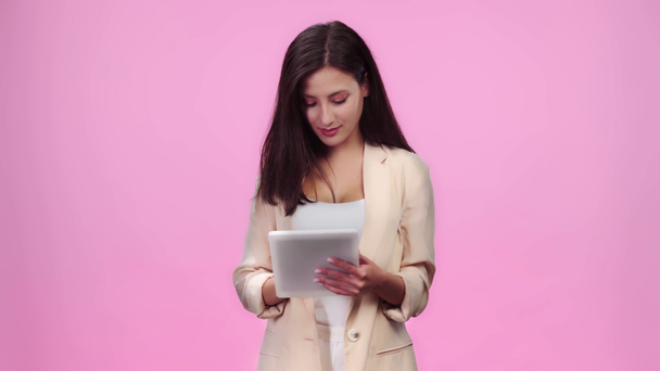 beautiful girl in formal wear using digital tablet and smiling isolated on pink - Metraje, vídeo