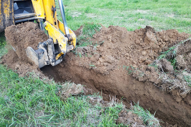 Baubagger gräbt eine flache Rinne für elektrische Leitungen oder Kabel. - Foto, Bild