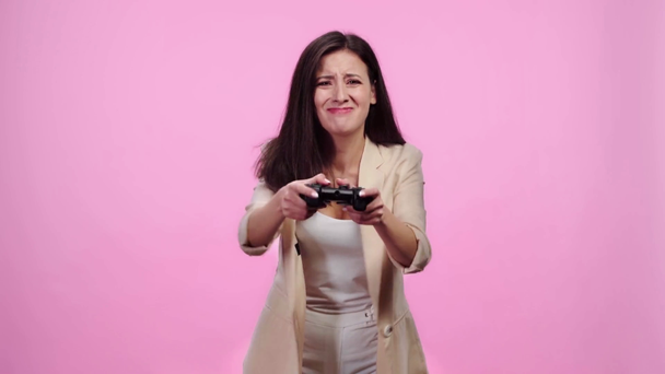 KYIV, UKRAINE - APRIL 8, 2019: upset girl in formal wear playing video game with joystick and throwing gamepad away isolated on pink - Кадри, відео