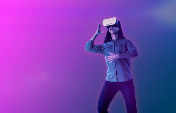 Woman gesturing while using virtual reality headset against gradient - Zdjęcie, obraz