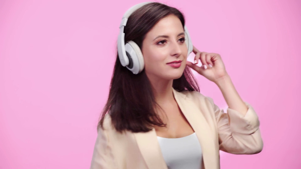 gyönyörű mosolygó lány fejhallgató smartphone hallgat zenét és a tánc izolált rózsaszín - Felvétel, videó