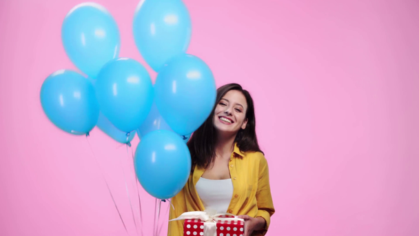 beautiful girl with gift holding balloons, looking at camera, cheering and smiling isolated on pink - Video