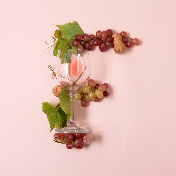 Alphabet. Letter F made of wineglasses with rose and white wine, grapes, leaves and corks lying on pink background. Wine degustation concept. Flat lay. Top view - Фото, зображення