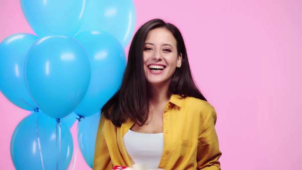 beautiful girl with gift holding balloons then looking at camera and smiling isolated on pink - Filmati, video