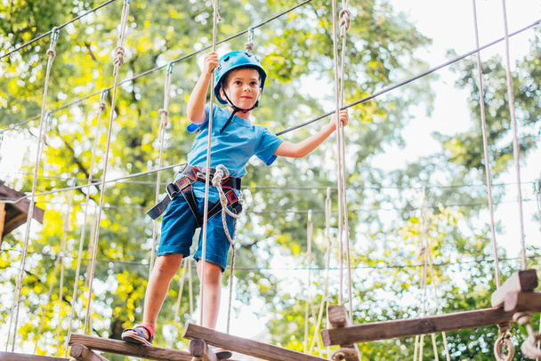 Little cute boy enjoying activity in a climbing adventure park on a summer sunny day.  Climbing extreme sport with helmet and insurance - Фото, зображення