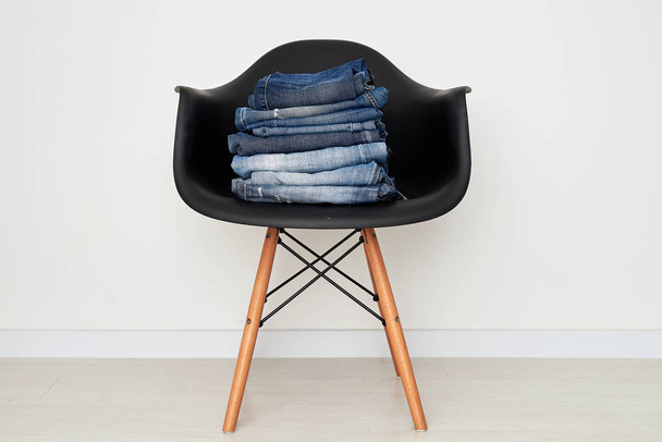 Jeans clothing stacked on a plastic chair - Zdjęcie, obraz