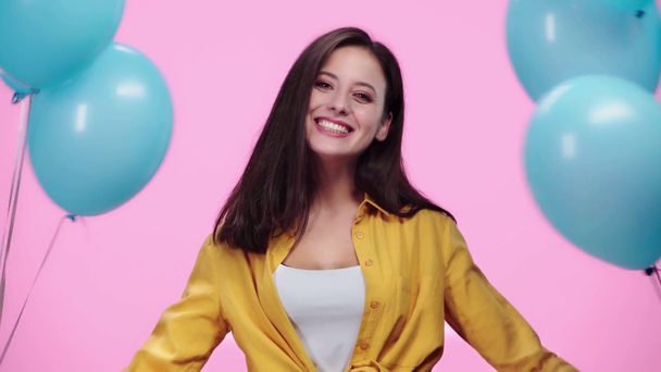 mooi meisje verstopt achter ballonnen dan kijken naar camera en glimlachend geïsoleerd op roze - Video