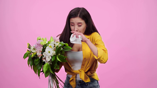 Uśmiechnięta dziewczyna wąchania kwiatów, kichanie i patrząc na kamerę izolowane na różowy - Materiał filmowy, wideo