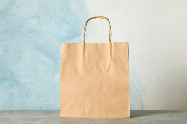 Paper bag on grey table against blue background, copy space - 写真・画像
