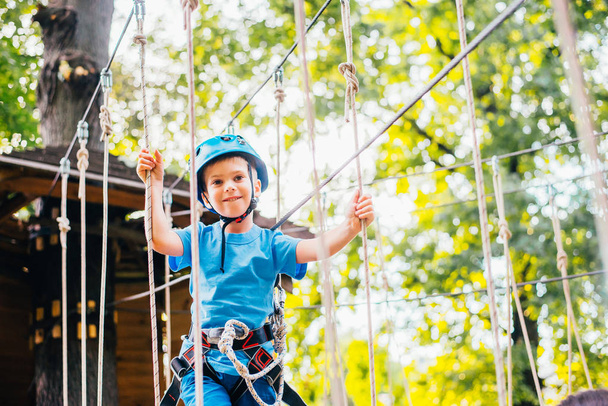 Little cute boy enjoying activity in a climbing adventure park on a summer sunny day.  Climbing extreme sport with helmet and insurance - Фото, зображення