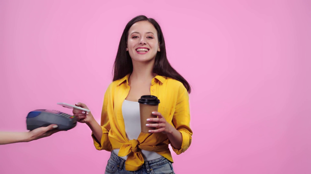 женщина держит платежный терминал в то время как счастливая девушка с кофе идти платить со смартфона изолированы на розовый
 - Кадры, видео