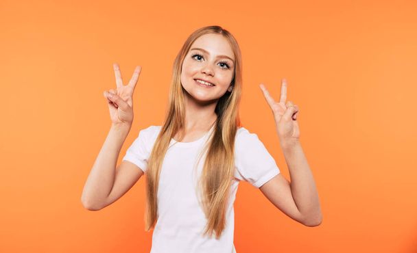 Happy winner. Very excited and happy beautiful little blonde girl in white t-shirt has a fun and posing and shouting isolated on yellow background. Signs and gestures concept. - Фото, изображение