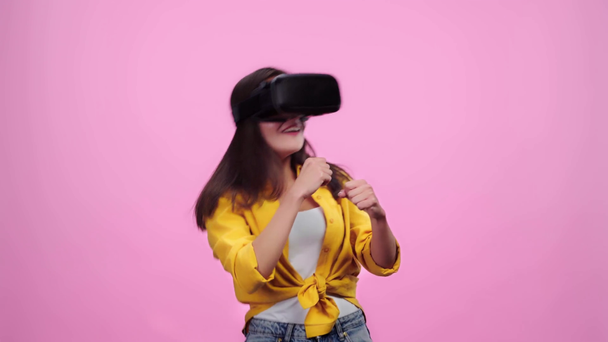excitada chica en auriculares de realidad virtual luchando con las manos cerradas aisladas en rosa
 - Metraje, vídeo