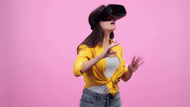 překvapená dívka ve virtuální realitě náhlavní souprava s gestikulovaným izolovaným růžovým - Záběry, video