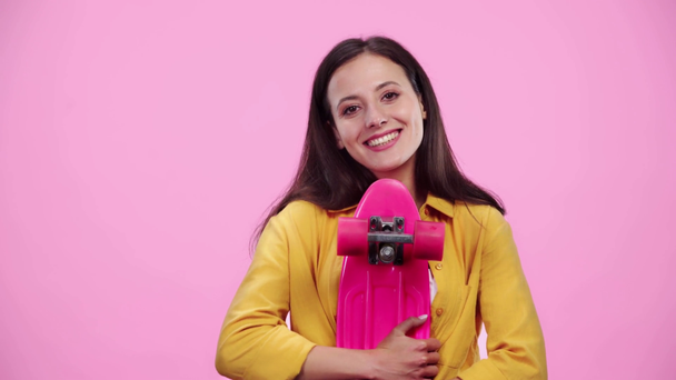 beautiful girl with penny board smiling and looking at camera isolated on pink - Filmati, video