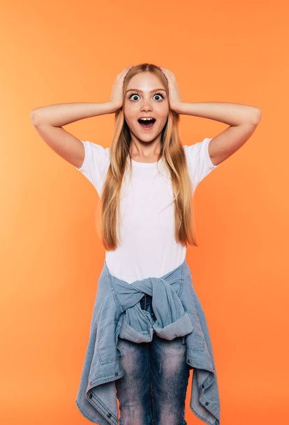 Happy winner. Very excited and happy beautiful little blonde girl in white t-shirt has a fun and posing and shouting isolated on yellow background. Signs and gestures concept. - Foto, Imagem