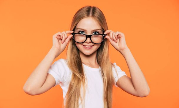 Close up portrait of happy, funny and beautiful blonde little girl in glasses is posing over yellow background. Study, education, school, university, college, graduate concept. - Foto, afbeelding