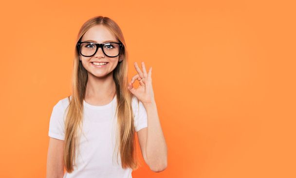 Close up portrait of happy, funny and beautiful blonde little girl in glasses is posing over yellow background. Study, education, school, university, college, graduate concept. - Фото, изображение