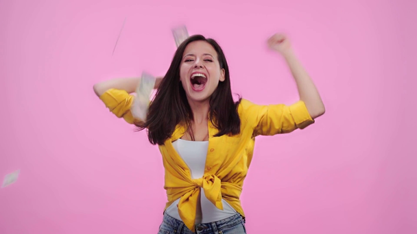 beautiful surprised girl looking at falling money, cheering with clenched hands and jumping isolated on pink - Imágenes, Vídeo