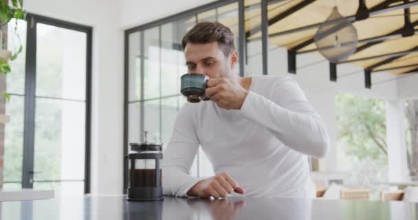 Front view of Caucasian man drinking coffee at dining table in a comfortable home. He is looking at coffee cup 4k - Felvétel, videó