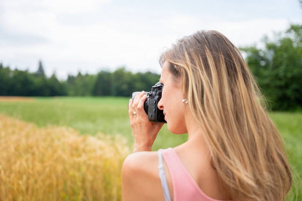 Young female photographer taking a photo of fields in nature - Фото, изображение