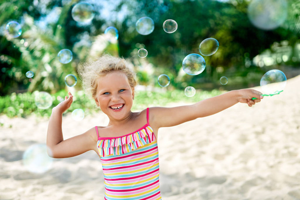 Pieni onnellinen tyttö leikkii saippuakuplia trooppisella rannalla. Lapsuus, elämäntapa käsite
 - Valokuva, kuva