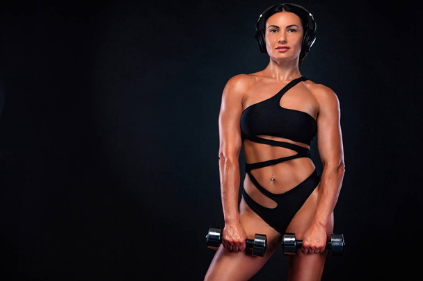Strong muscular bodybuilder athletic woman pumping up muscles with dumbbells on black background. Workout bodybuilding concept. - Foto, immagini