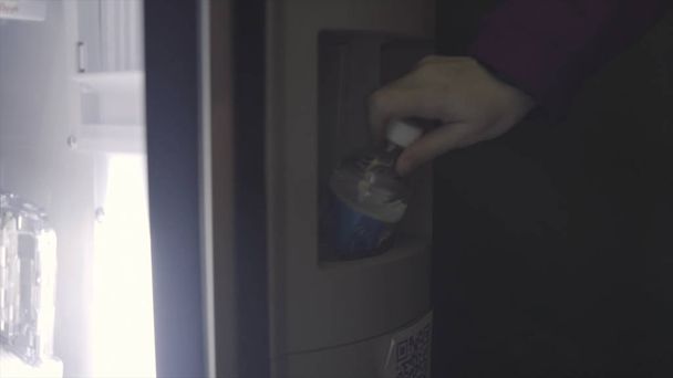 Seitenansicht einer Frau, die eine Flasche Wasser aus einem Automaten nimmt. Kunst. Verkaufsautomat mit einer großen Auswahl an alkoholfreien Getränken und Tee. - Foto, Bild